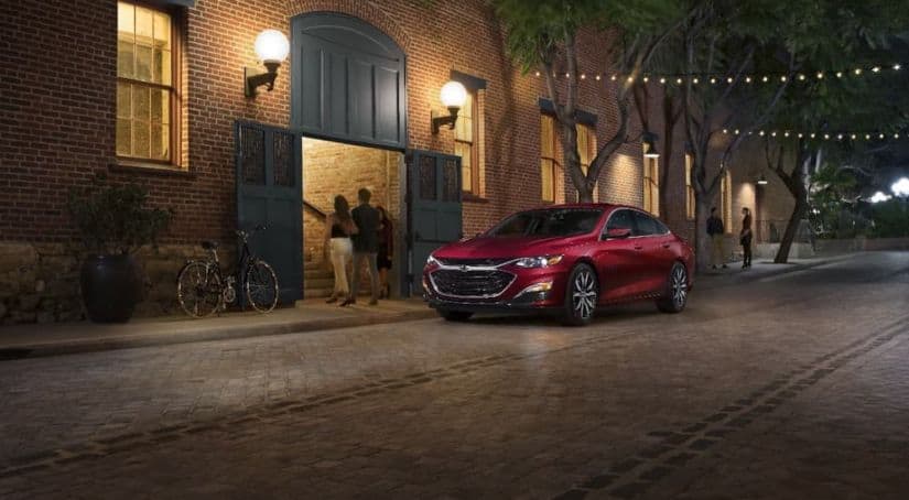A red 2021 Chevy Malibu is parked in front of a tan brick building.