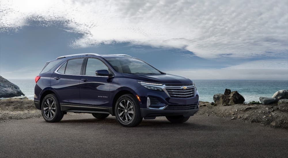 A dark blue 2022 Chevy Equinox, coming soon to a GM dealer near you, is parked in front of a cloudy blue sky.
