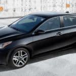 A black 2021 Kia Forte is in a cement parking area after leaving a Kia dealer.