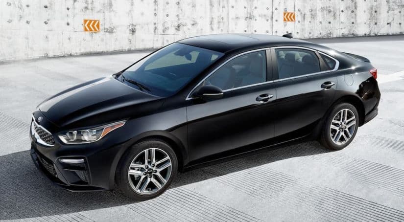 A black 2021 Kia Forte is in a cement parking area after leaving a Kia dealer.