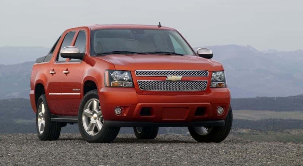 An orange 2011 Chevy Avalanche is parked in front of distant mountains.