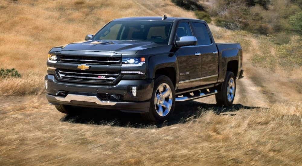 A black 2018 Chevy Silverado 1500 is driving off-road on a path through dry grass.