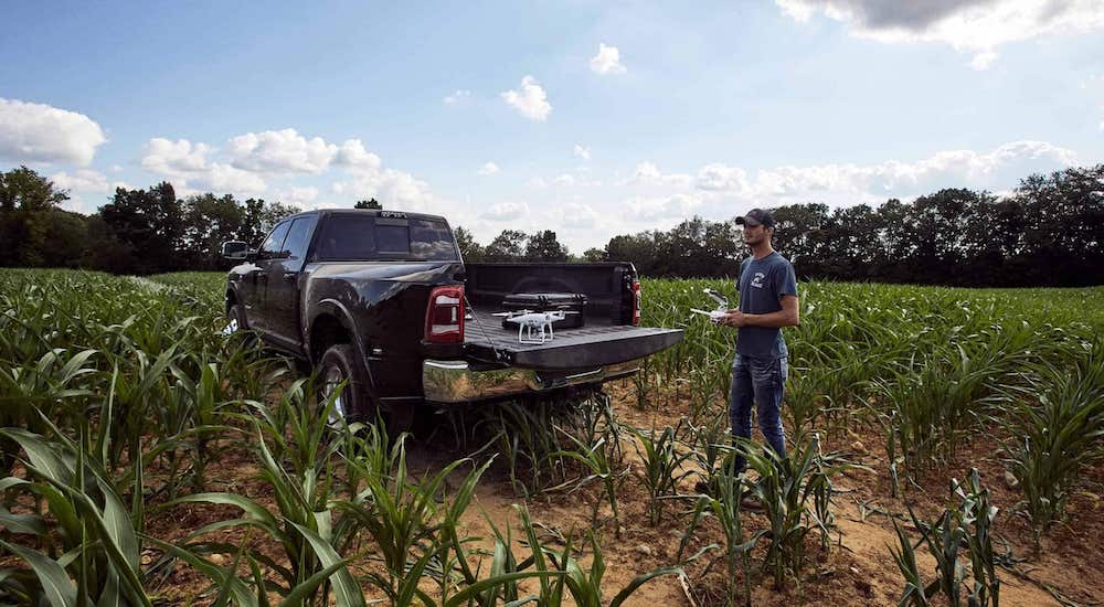 A black 2020 Ram 3500 is parked on a field with a man operating a drone from the bed of the truck.