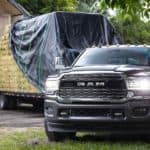 A black 2020 Ram 3500 is parked in front of a barn with a trailer full of hay bales.