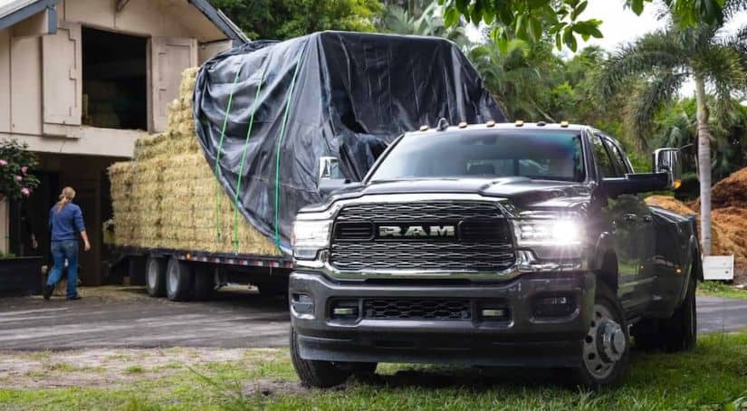 A black 2020 Ram 3500 is parked in front of a barn with a trailer full of hay bales.