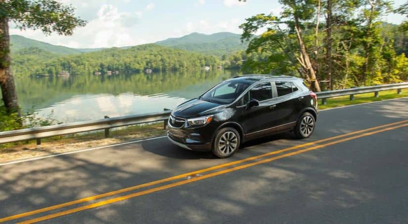 A black 2021 Buick Encore is driving down the road past a lake.