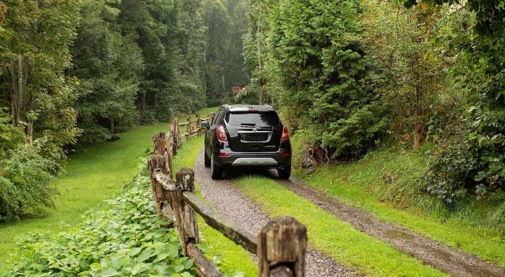 A black 2021 Buick Encore is shown from the rear driving up a trail towards a cabin in the woods.
