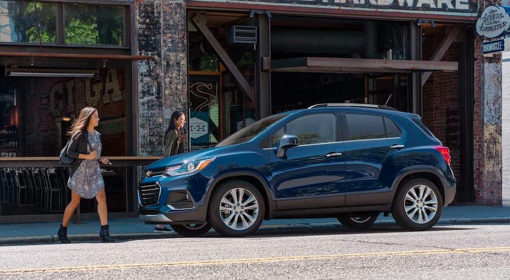 A blue 2021 Chevrolet Trax is parked in front of a store with two women approaching it.