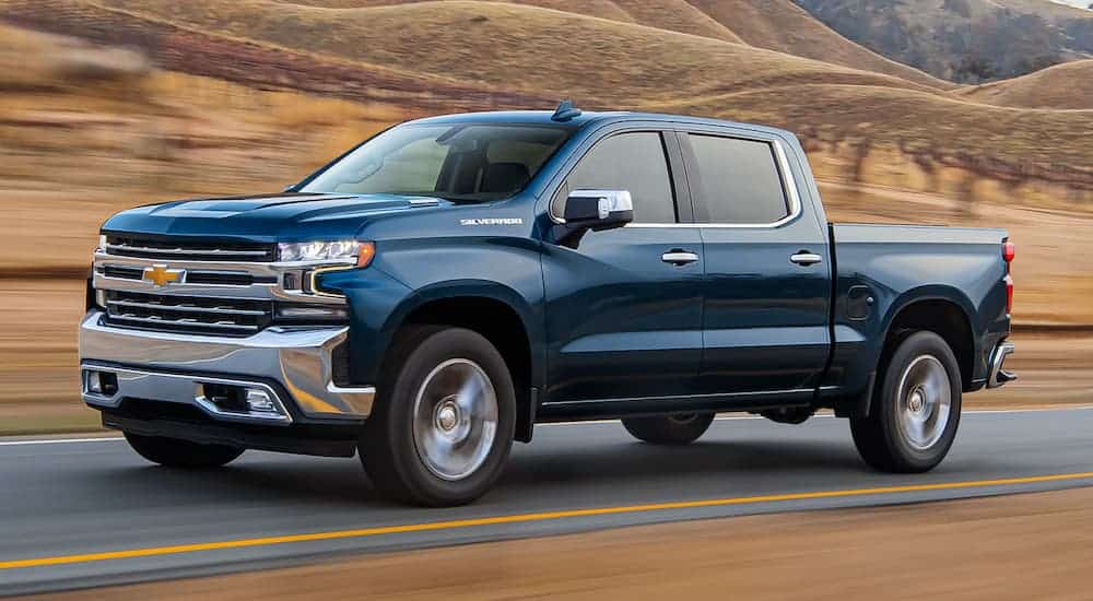 A blue 2021 Chevy Silverado is shown in profile driving down the highway with a blurred field in the background.