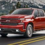 A red 2021 Chevy Silverado 1500 is driving down the highway with snowy mountains in the background.