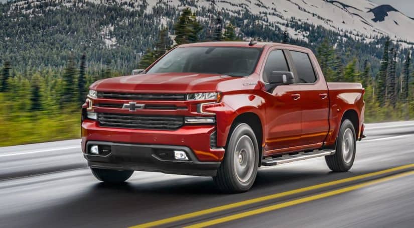 A red 2021 Chevy Silverado 1500 is driving down the highway with snowy mountains in the background.