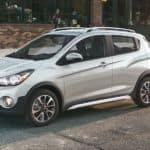 A silver 2021 Chevy Spark is parked in front of a brick building.