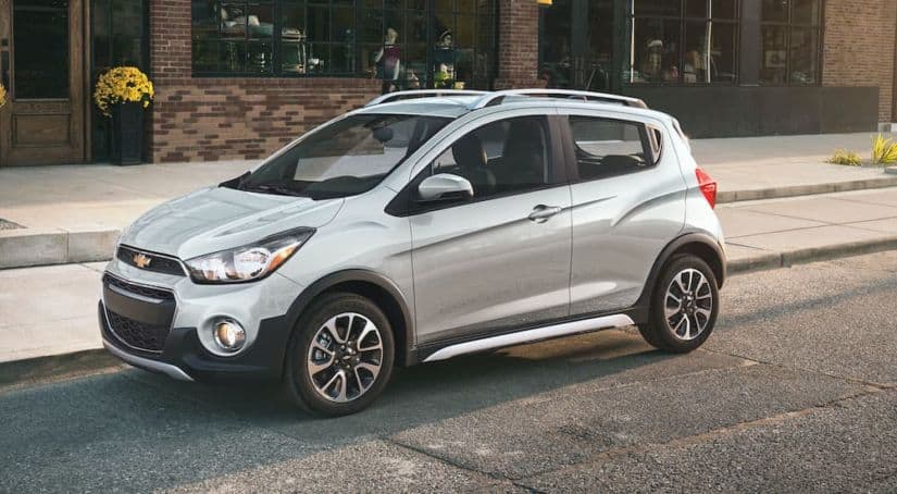 A silver 2021 Chevy Spark is parked in front of a brick building.
