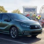 A green 2021 Honda Odyssey is parked in front of a county fair and ferris wheel.