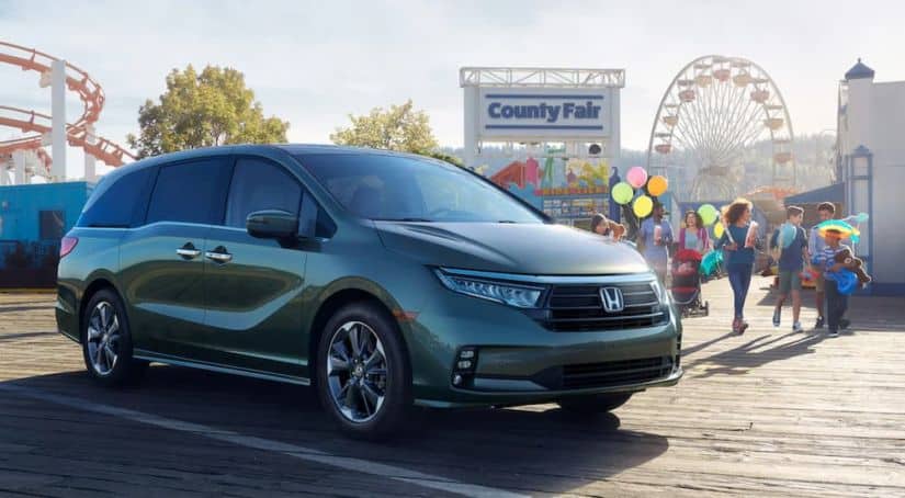 A green 2021 Honda Odyssey is parked in front of a county fair and ferris wheel.
