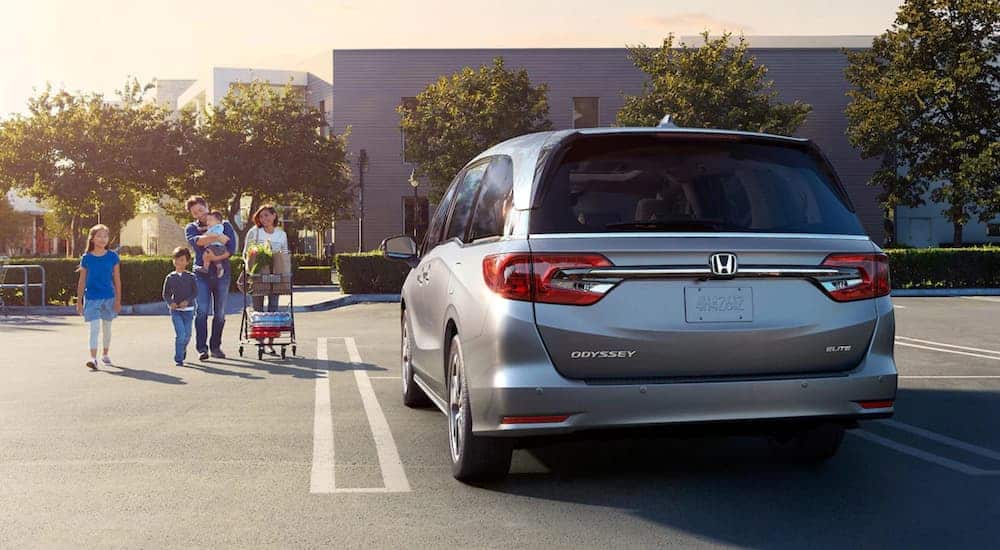 A silver 2021 Honda Odyssey is parked outside a grocery store with a family approaching it.