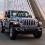 A silver 2021 Jeep Wrangler is driving across a modern cable bridge.