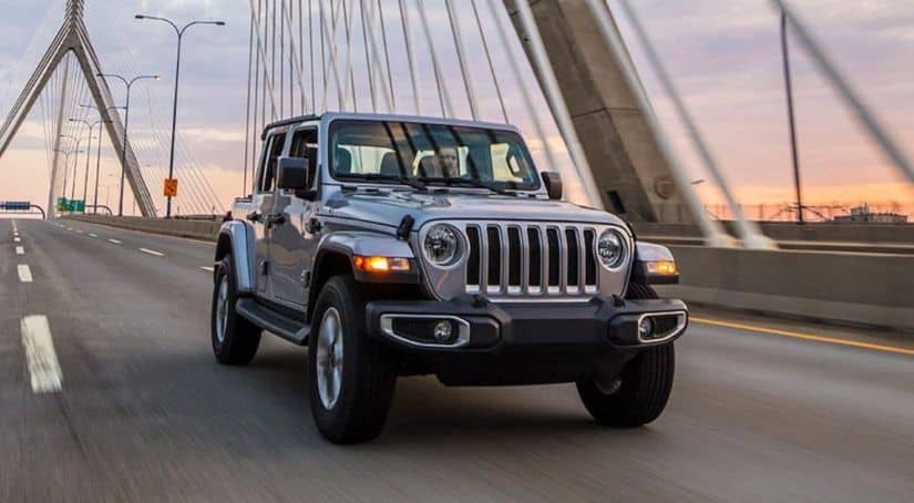 A silver 2021 Jeep Wrangler is driving across a modern cable bridge.