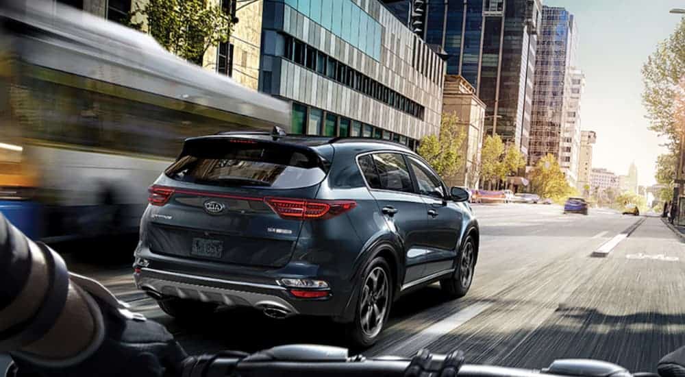 A blue 2021 Kia Sportage is driving through the city with a biker behind it.