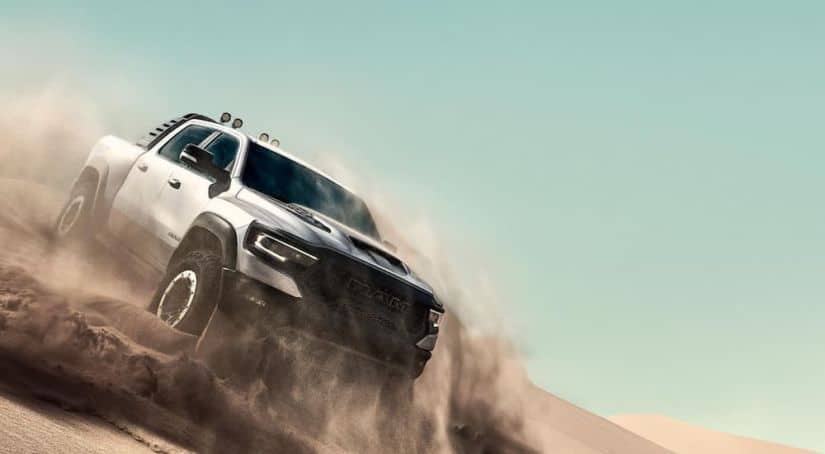 A silver 2021 Ram 1500 TRX is sliding down a desert hill kicking up dust, showing you what Ram trucks are all about.