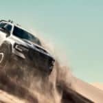 A silver 2021 Ram 1500 TRX is kicking up sand while driving down a sand dune.