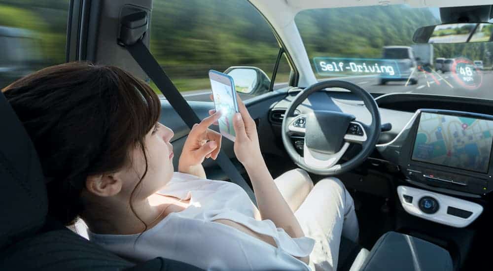 A woman is looking at her cell phone in the driver seat while being transported by a self driving vehicle.