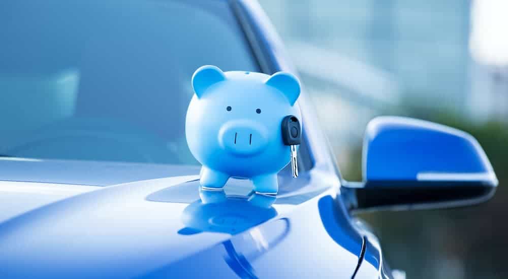 A blue piggy bank with a key is sitting on a blue sedan at a Bad Credit Car Lot in Kansas City.