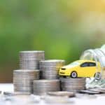 A yellow toy car is partially sitting in a glass jar with a bunch of quarters.