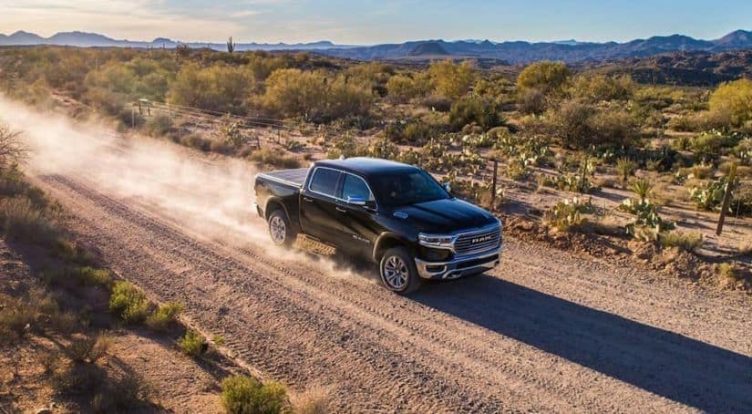 A black 2019 used Ram 1500 is driving down a dirt road kicking up some dust.