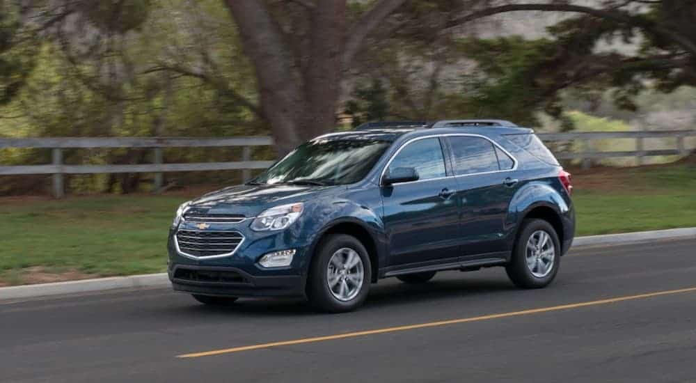 A blue 2016 used Chevy Equinox LT is driving down the road past a fence and trees.
