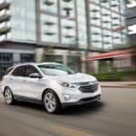 A white 2018 used Chevy Equinox is driving past blurred modern buildings.