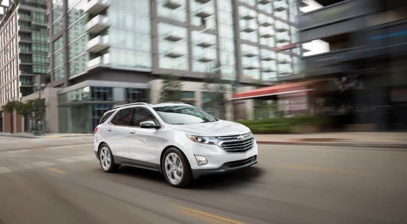 A white 2018 used Chevy Equinox is driving past blurred modern buildings.