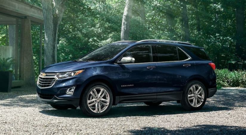 A blue 2020 Chevy Equinox is parked on a gravel driveway at a home in the woods.