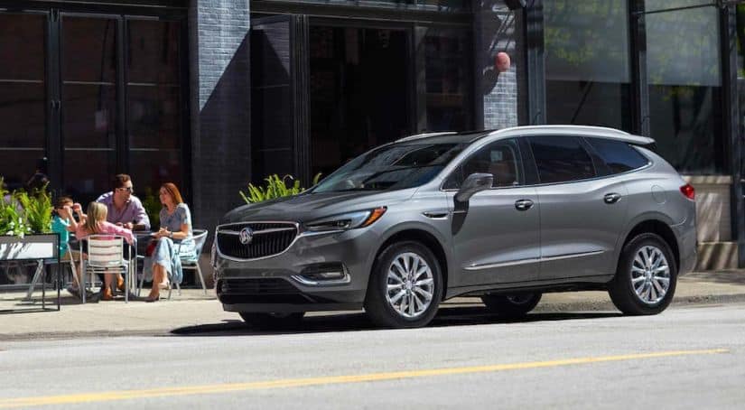 A family is sitting at a table next to a gray 2021 Buick Enclave that is parked on a street.