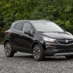 A black 2021 Buick Encore is parked in an empty lot in front of trees after winning the 2021 Buick Encore vs 2021 Chevy Trax comparison.