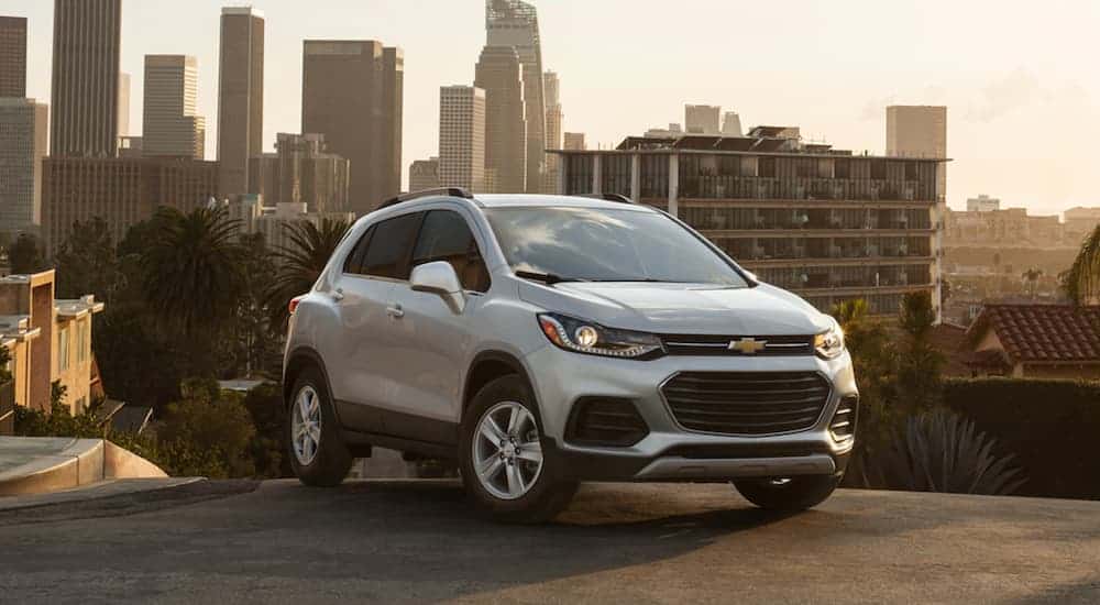 A white 2021 Chevy Trax is parked in front of a city at sunset.