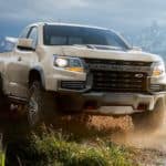 A tan 2021 Chevy Colorado ZR2 is driving on a dirt road in front of distant mountains.