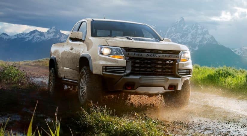 A tan 2021 Chevy Colorado ZR2 is driving on a dirt road in front of distant mountains.