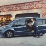 Two people are loading planters and plants into the side of a blue 2021 Ford Transit Connect van.