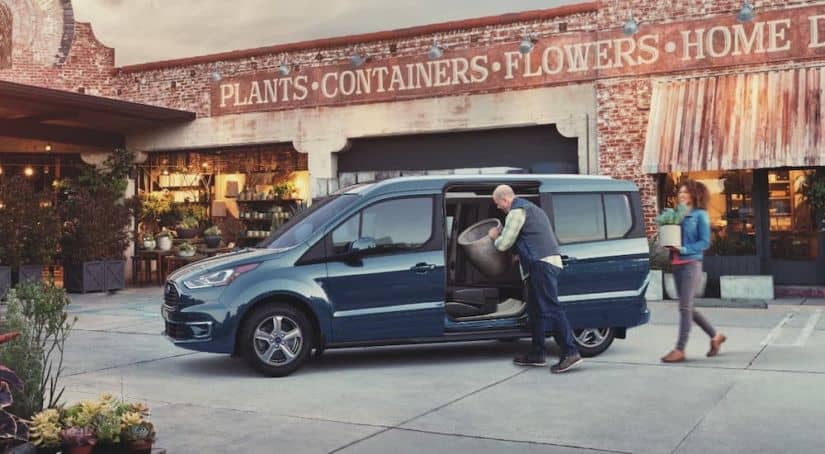 Two people are loading planters and plants into the side of a blue 2021 Ford Transit Connect van.