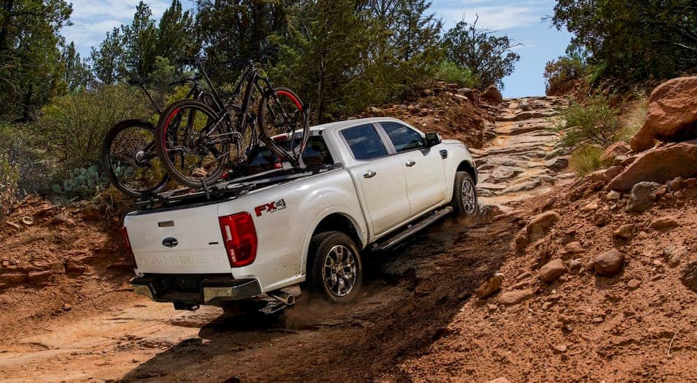 A white 2021 Ford Ranger Lariat is driving up a dirt hill with mountain bikes mounted over the bed.