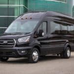 A black 2021 Ford Transit Passenger van is parked in front of a glass building.