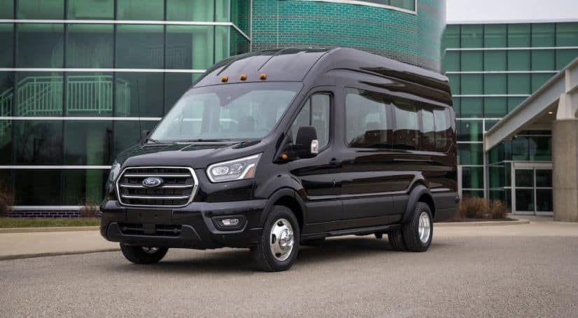 A black 2021 Ford Transit Passenger van is parked in front of a glass building.