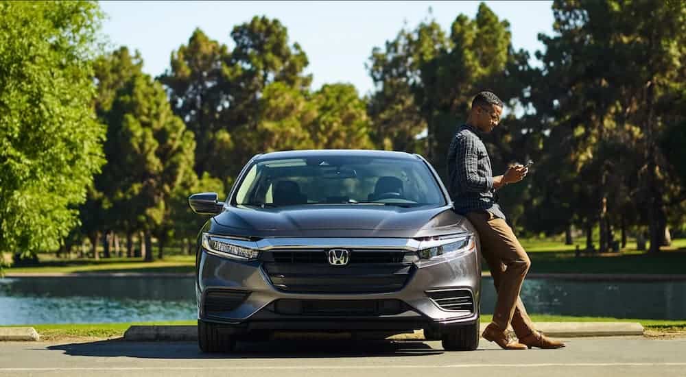 A grey 2021 Honda Insight LX is parked with a man leaning against it looking at his phone.