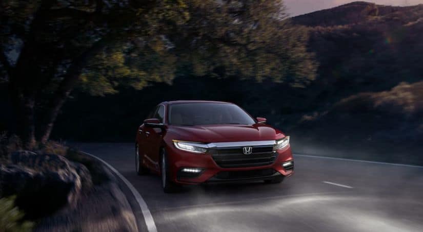 A red 2021 Honda Insight Touring is driving down the road at night with its headlights on.
