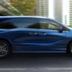 A blue 2021 Honda Odyssey Touring is driving down a highway through the city.