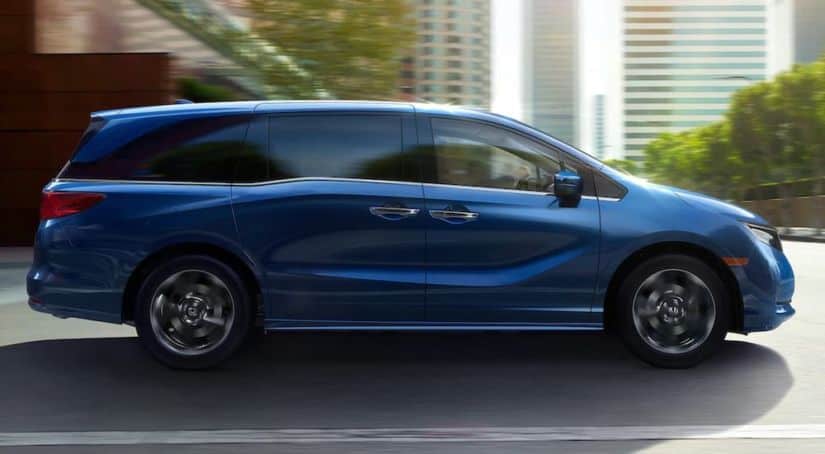 A blue 2021 Honda Odyssey Touring is driving down a highway through the city.
