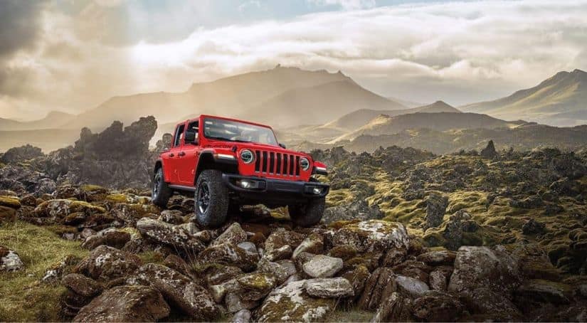 A red 2021 Jeep Wrangler Rubicon Unlimited is parked on a rocky hill with misty mountains in the background.