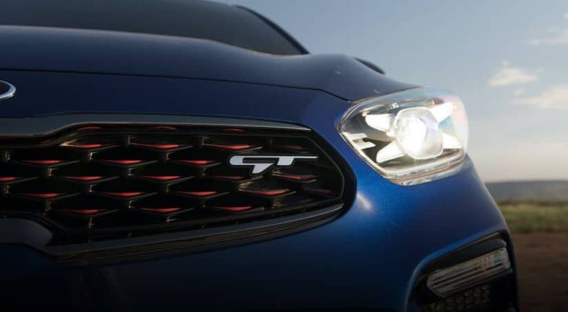 A close up of the front driver side headlight and grille on a blue 2021 Kia Forte GT.