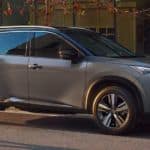 A grey 2021 Nissan Rogue is shown in profile parked in front of a building.